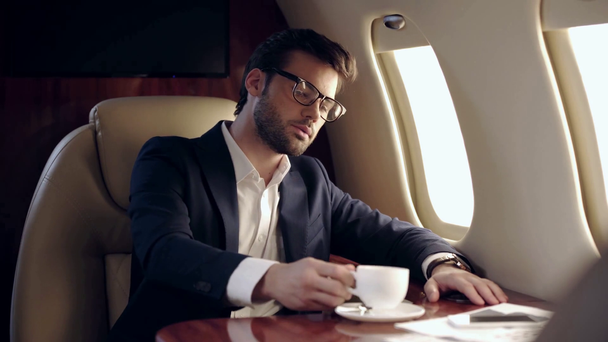 pewny siebie biznesmen pijący kawę podczas podróży samolotem - Materiał filmowy, wideo