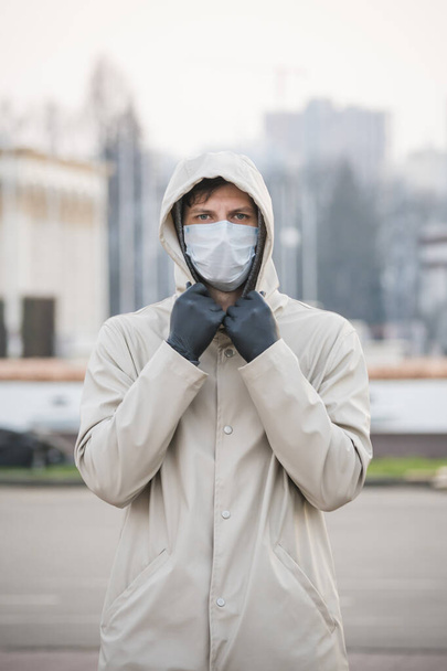 Close-up portrait young europeans man in protective disposable medical face mask walking outdoors. New coronavirus (COVID-19). Concept of health care during an epidemic or pandemic - Photo, Image