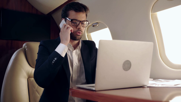 серйозний бізнесмен, який друкує на ноутбуці і розмовляє на смартфоні в літаку
 - Кадри, відео