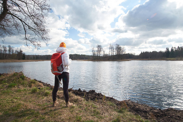 woman traveler observes early spring lake while traveling, view from back - Photo, Image