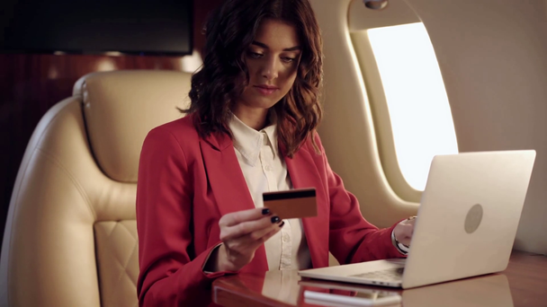 młoda businesswoman za pomocą laptopa, trzymając kartę kredytową w samolocie - Materiał filmowy, wideo