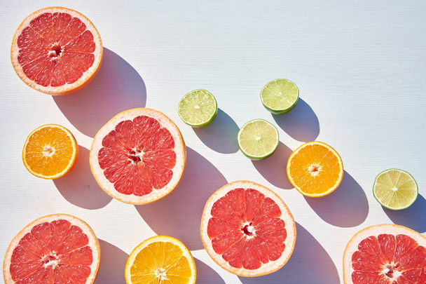 Packed ripe orange, grapefruit and lime halves packed on white wooden background, close-up shot from above in harsh sunlight with long colored shadows. - Fotó, kép