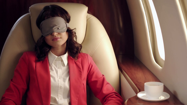 atrakcyjne businesswoman zakładanie maski snu podczas podróży samolotem - Materiał filmowy, wideo