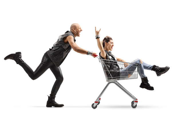 Full length profile shot of a punk pushing a woman inside a shopping cart isolated on white background - Valokuva, kuva