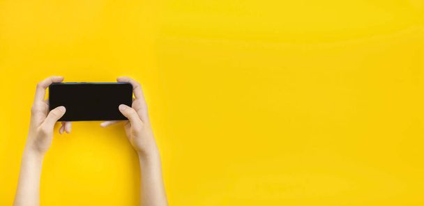 Ein Mann hält auf gelbem Hintergrund ein Smartphone in der Hand. Moderner Lebensstil. Unternehmen. Ansicht von oben. Banner. Kopierraum. - Foto, Bild