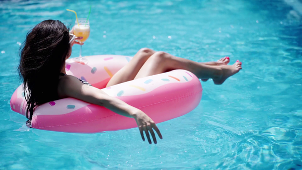 brunetka dívka v slunečních brýlích s koktejlem plavání na koblize plavecký kroužek - Záběry, video