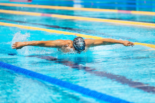 Sportovní muž plavání ve stylu motýla v bazénu s průzračnou modrou vodou. - Fotografie, Obrázek