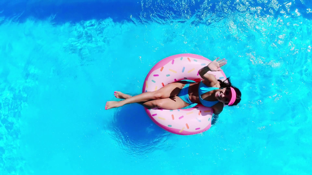 widok góry szczęśliwy dziewczyna macha ręką na pierścień pączek pływacki w basenie - Materiał filmowy, wideo