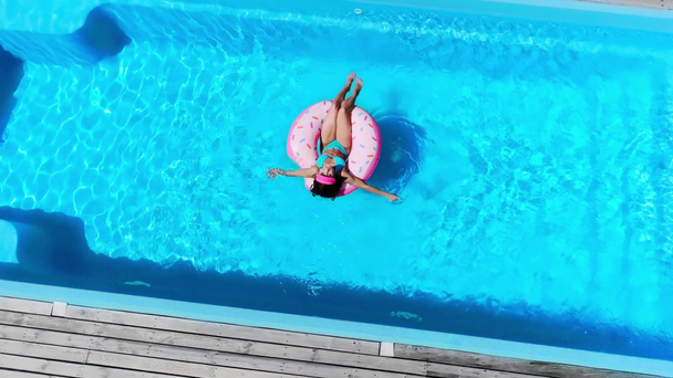 bovenaanzicht van vrouw op donut zwemring in zwembad in de zomer - Video
