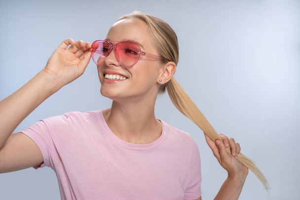 Positive delighted longhaired blonde touching her glasses - Photo, Image