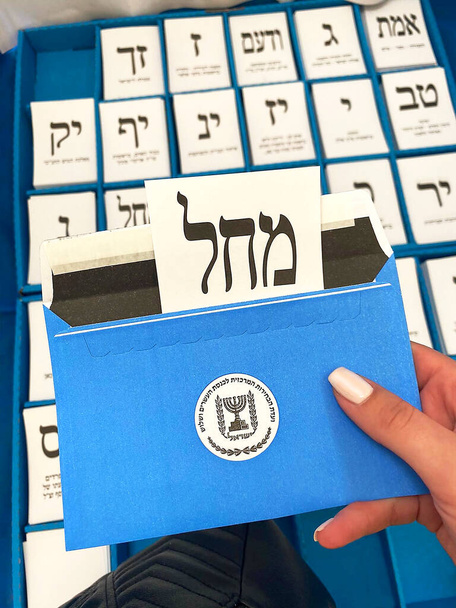 ženská ruka drží obálku s hlasovacím lístkem na různých hlasovacích lístcích různých izraelských politických stran. Text v hebrejštině. Volby do Izraele - Fotografie, Obrázek