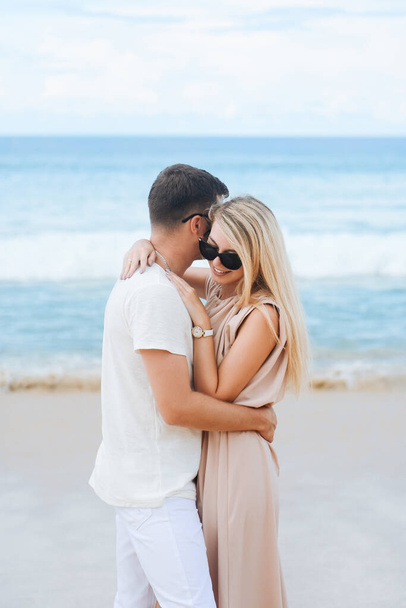 Giovane attraente uomo e donna innamorati camminano e si abbracciano sullo sfondo di sabbia bianca e mare azzurro. Viaggio, luna di miele
 - Foto, immagini