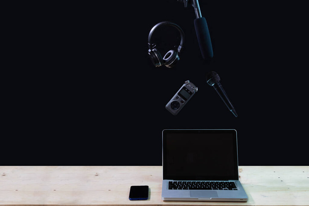 Laptop, fejhallgató, telefon és kamera tartozék fekete háttérrel. Hordozható laptop fejhallgatóval és mini sztereó mikrofonnal színes fa háttéren. Modern eszközök, hangfelvétel koncepció. - Fotó, kép