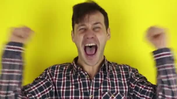 Funny, handsome guy, actively expresses joy, screams, laughs and enjoys winning the lottery. Portrait of a young guy, he laughs and actively expresses joy. Portrait on a yellow background. - Video