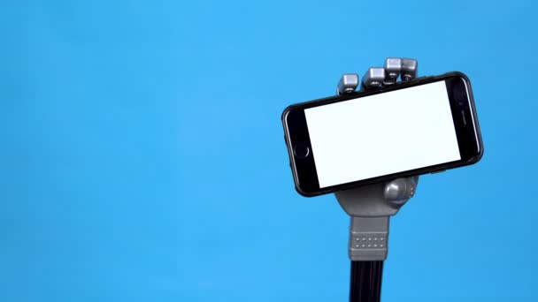 Una mano mecánica sostiene un teléfono con una pantalla blanca. Mano cyborg gris sosteniendo un smartphone sobre un fondo azul. Plantilla
. - Metraje, vídeo