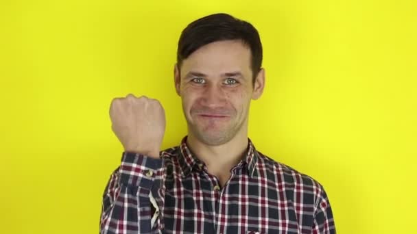 A funny, handsome guy says yes and makes a hand gesture expressing victory. Portrait of a young guy, he says yes and makes a hand gesture expressing the achievement of the desired result. Portrait on a yellow background. - Video, Çekim