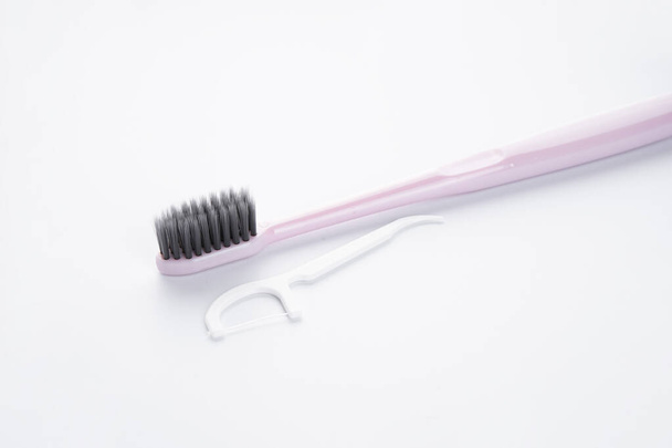 Rosafarbene Zahnbürste mit weißem Zahnstocher und Zahnseide auf weißem Hintergrund. - Foto, Bild