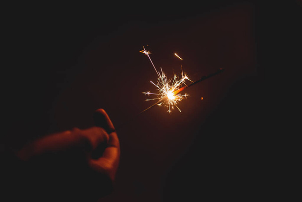 Brandende vonkstok starlight vuurwerk pyrotechnisch donker zwart warme achtergrond bij de hand gehouden - Foto, afbeelding
