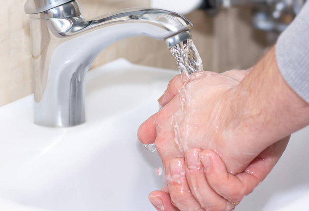 Ein Mann wäscht sich unter fließendem Wasser die Hände. Nahaufnahme. Gesundheits-, Sauberkeits- und Hygienekonzept. - Foto, Bild