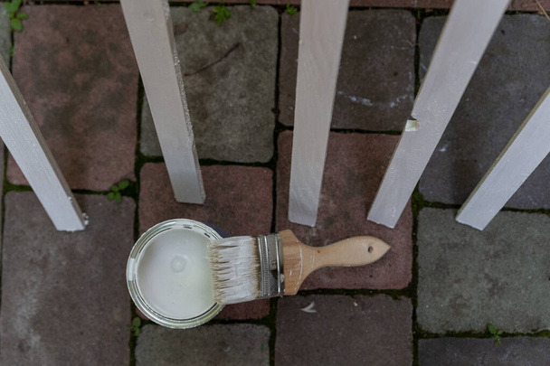 пензлик покритий білою фарбою і баночкою з розфарбованих смуг на темному фоні
 - Фото, зображення