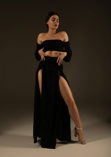 Elegant beautiful woman with long legs in black fashionable dress posing in studio on grey background. - Foto, Imagen
