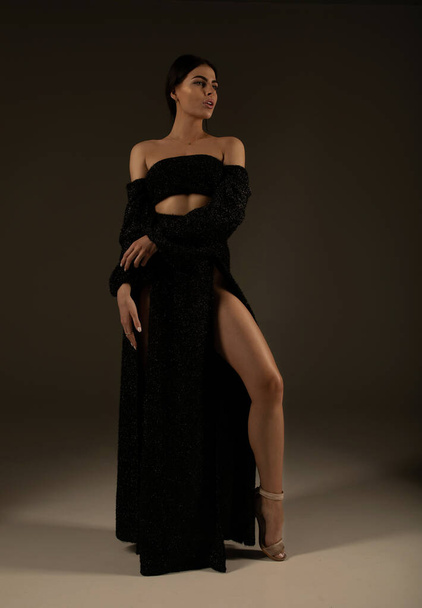 Elegant beautiful woman with long legs in black fashionable dress posing in studio on grey background. - Фото, изображение