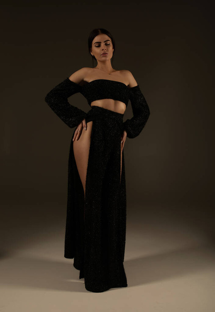 Elegant beautiful woman with long legs in black fashionable dress posing in studio on grey background. - Foto, Imagem