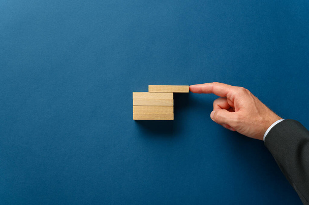Finger of a businessman pushing top wooden peg in a stack of them in line with the others.  Conceptual image of business strategy and start up.  - Photo, Image