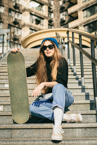 Urban woman with skate. Hipster girl with skateboard in city. Extreme sport and emotions concept. Alternative lifestyle. Stylish hipster girl holding skateboard and posing. Street style outfit. - Fotoğraf, Görsel
