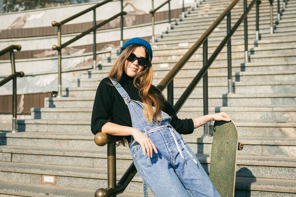 Urban woman with skate. Hipster girl with skateboard in city. Extreme sport and emotions concept. Alternative lifestyle. Stylish hipster girl holding skateboard and posing. Street style outfit. - Photo, Image