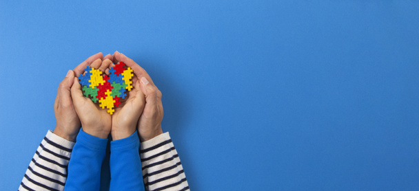 Conceito do dia da consciência do autismo mundial. Adulto e criança mãos segurando coração quebra-cabeça no fundo azul claro - Foto, Imagem