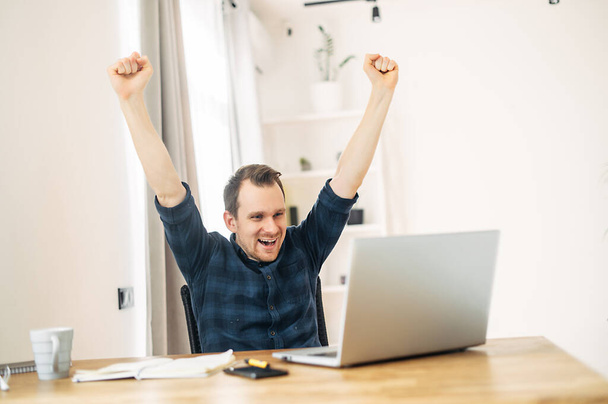 A man looks at laptop and rejoices at job success - Foto, afbeelding