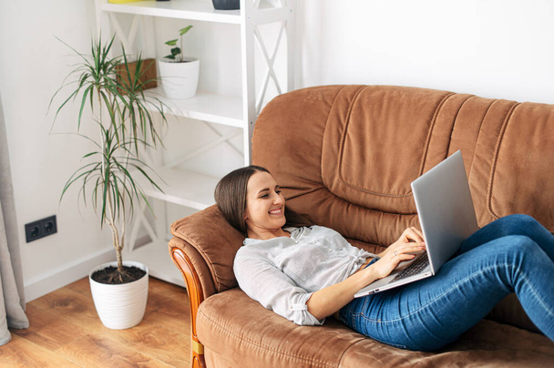 A woman is lying at home on the sofa with a laptop - Foto, Bild