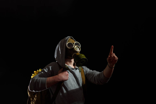 Людина в газовій масці з квітами в рюкзаку. Екологічне забруднення, охорона природи, екологічна катастрофа та концепція надії. Чорний фон, простір копіювання
. - Фото, зображення