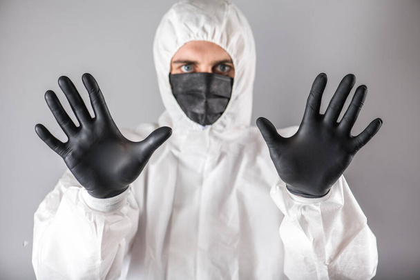 a virologist in protective suit with a respirator face mask and black gloves with fear on face shows stop sign by hands into camera. collapse of health care system due to epidemic coronavirus. - Φωτογραφία, εικόνα