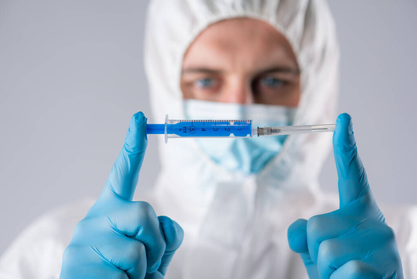virologist in protective suit with respirator face mask and blue gloves holds a syringe - Foto, Bild