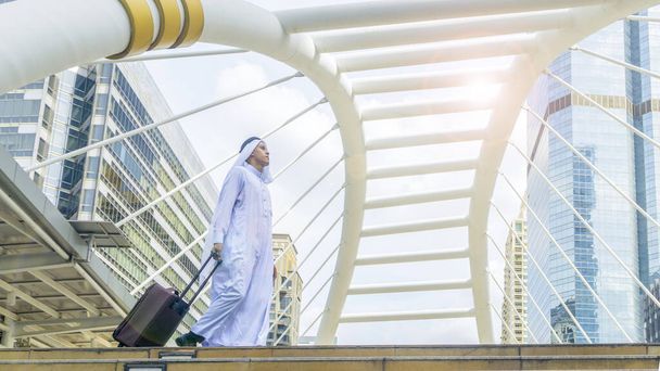 Business arab traveler saudi man carrying a suitcase and walk in the business landmark city with the modern steel structure and exterior wall modern building  - Foto, Imagem
