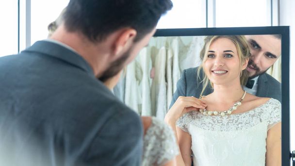 groom man and woman bride wearing jewelry necklace in feeling in happy love and looking on reflective glass in fitting room. - Photo, Image