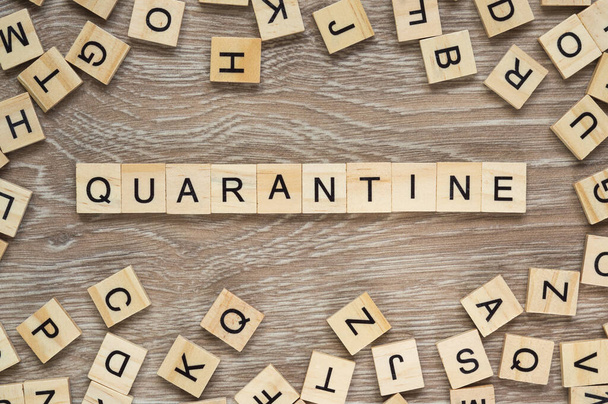 The word "Quarantine" spelt out with letter tiles on the wooden background - Zdjęcie, obraz