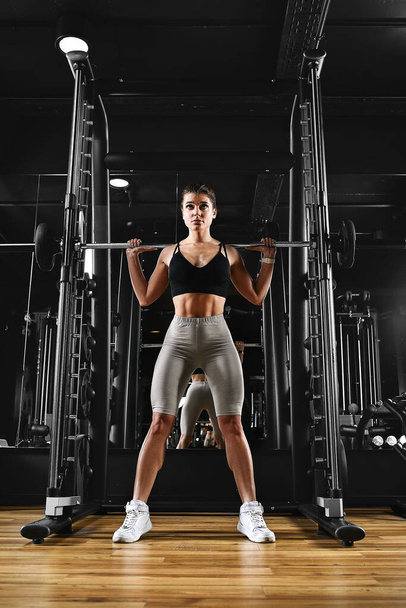 A girl is training her legs in the gym with a barbell. Sport lifestyle, keep fit, fitness motivation. dark background, copy space - Foto, Imagem