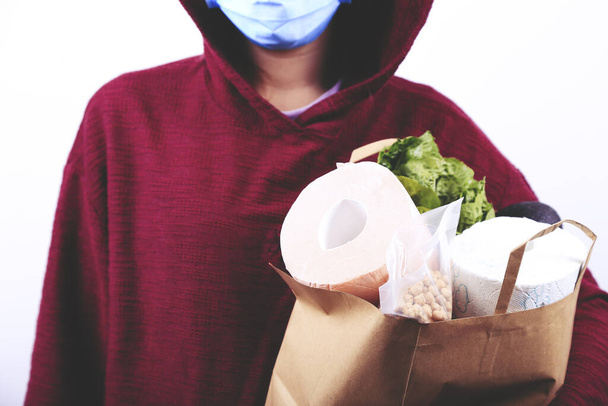 Girl in protective mask is holding paper bag with food and toilet paper. Coronavirus outbreak. Panic. - Photo, Image
