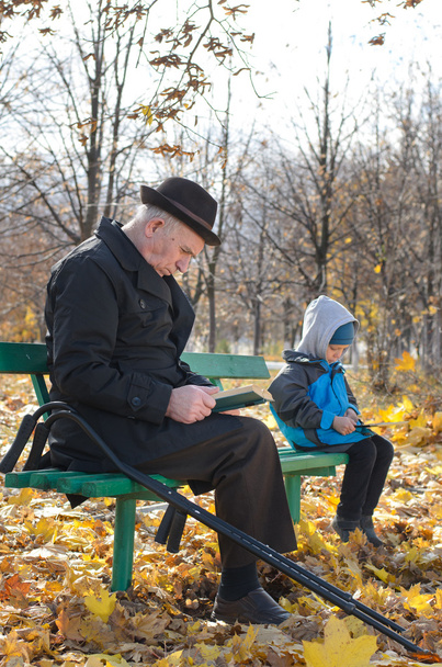 Eläkkeellä oleva mies lukee puistossa pojanpoikansa kanssa.
 - Valokuva, kuva