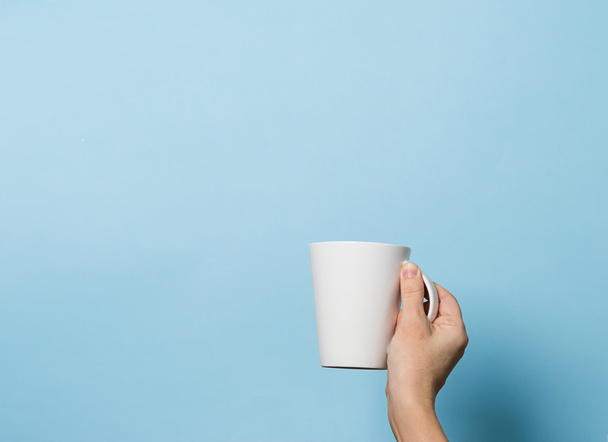 女性は彼女の手の中にコーヒーや紅茶を飲む青の明るい背景のカップを保持しています。フードドリンクのコンセプト。スペースのコピー. - 写真・画像
