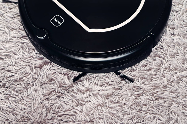 Aspiradora automática robot en negro sobre una alfombra shag gris. Nuevas tecnologías modernas para la limpieza de apartamentos. asistente electrónico del hogar inteligente
 - Foto, imagen