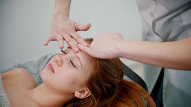 Masáž - žena masérka masírující obličej zrzavé ženy rukama - Záběry, video