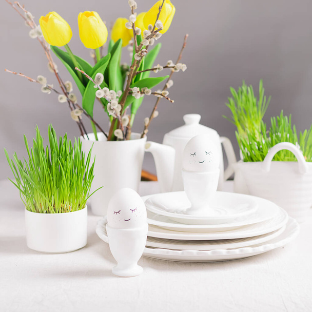 Kutlama kompozisyonu, gözlüklü Paskalya yumurtaları beyaz tabaklar ve beyaz bir masada söğüt laleleri. Mutlu Paskalyalar. - Fotoğraf, Görsel