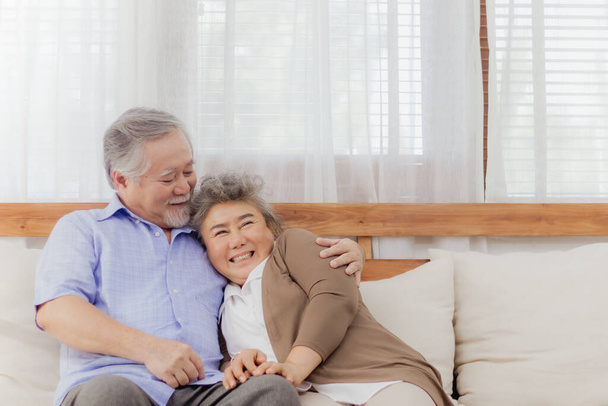 Happy Asian senior couple stay together on sofa at home in romantic moment. Retired lovely elderly smiling grandparent lover hugging, embracing with love and holding hands. Retirement life of older - Φωτογραφία, εικόνα