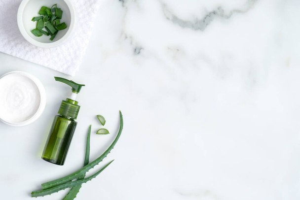 Aloe vera spa treatment concept. Top view green bottle with aloe vera gel, hand cream and sliced stems aloe vera on marble background. Organic natural skincare products - Foto, imagen