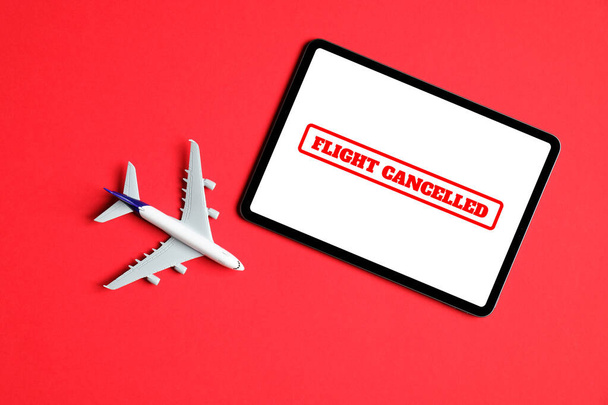 Plane model and tablet with text "flight cancelled" on a screen over red background. Flight cancellation due to the impact of coronavirus (COVID-19) concept. - Photo, Image