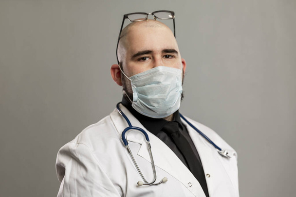 Male doctor in a white coat and mask. Gray background. Close-up. Coronavirus pandemic. - Фото, зображення